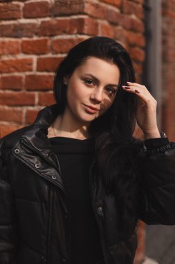 Esmer saçlı modacı kız dışarıda poz veriyor. Deri ceketli kadın saçını düzeltiyor, sokakta yürüyor. Şehirde poz veren mutlu turist kadın. İyimser bayan dışarı çıkıyor..