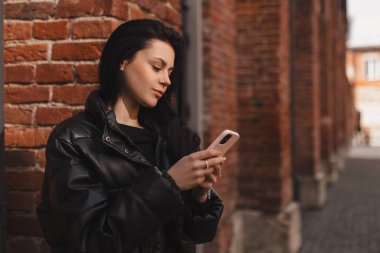 Mutlu esmer kadın, dışarıdaki tuğladan duvarları izole edip sosyal ağda cep telefonuyla sohbet ediyor. Aktif şehir gençliği kavramı. Kız cep telefonunu tutar, sohbet eder, mesajlaşır, haberleri okur..