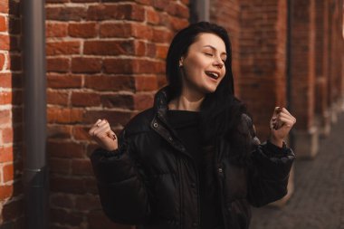 Neşeli, güzel bir kadın kutlama yapıyor, inançsızlık ve heyecanla kazanan bir ödül olarak bakıyor, şampiyon gibi tezahürat yapıyor, iyi haberlerden ve zaferden bağırıyor, dışarıda duvarın yanında duruyor, kapalı gözler.