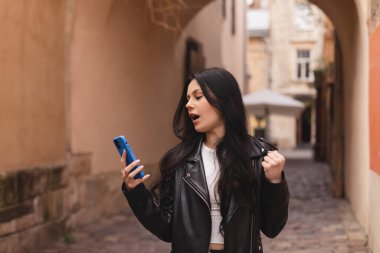 Sokakta yürüyen hayret verici bir kadın, mutlu cep telefonu, gülümseme, kazanma hareketi. Sokaktaki esmer kadın mesajları okuyor ve mutlu görünüyor, kutlama yapıyor, başarı, vay canına duyguları. İyi alışveriş..
