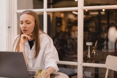 Yorgun ya da düşünceli, yorgun, yorgun ve serbest çalışan güzel bir kadın. Açık kafede dizüstü bilgisayarı üzerinde çalışıyor. Kafasını elleriyle tutuyor. Çok çalışma, son teslim tarihi, kötü haber konsepti. Çözümleri düşün..