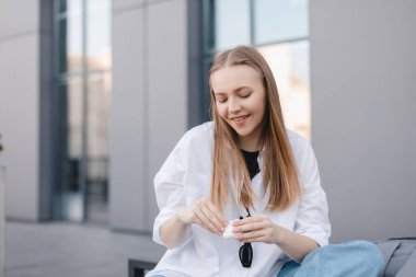 Ofisin yanındaki bankta oturan mutlu sarışın kadın ve kulaklık kutusundan kablosuz kulaklıkları çıkarıyor. Kız müzik dinlemek ya da kulaklık kullanarak cep telefonuyla konuşmak istiyor. Mutlu iş kızı.