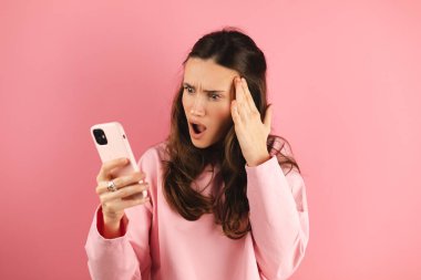 Pembe arka planda izole edilmiş cep telefonu kullanan genç ve güzel bir kadın. Bağıran mutsuz kadın cep telefonunu tutuyor. Hayal kırıklığına uğramış üzgün bayan, haberleri dehşete düşürdü. Bu da ne? Olamaz..