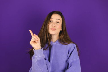 Bak, buraya ilan ver! Koyu renk saçlı, çekici gülüşü olan güzel bir kadın, iyi bir anlaşmaya olumlu bir yaklaşım sergiliyor, tavsiyesini belirtirken, mor arka planda sol tarafı işaret ediyor..