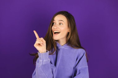 Bak, buraya ilan ver! Koyu renk saçlı, çekici gülüşü olan güzel bir kadın, iyi bir anlaşmaya olumlu bir yaklaşım sergiliyor, tavsiyesini belirtirken, mor arka planda sol tarafı işaret ediyor..