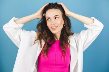 Sevimli esmer kadın, şakacı bir şekilde göz kırpıyor, flört ediyor, saçlarını savuruyor. Kadın saçını düzeltiyor. Esmer, manken suratlı, gülümseyen. Pembe bluzlu kız, mavi arka planda beyaz gömlek..