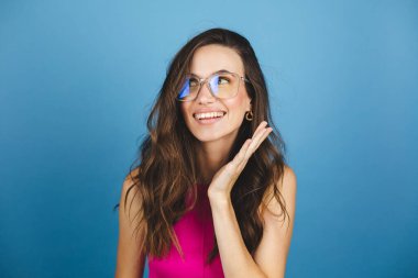 Genç esmer, kıvırcık kadın portresinin yakın plan portresi pozitif görünüm, büyük gülümseme, stüdyoda mavi arka planda poz veren güzel bir model. Kız pembe bluz ve gözlük takıyor. Benim..