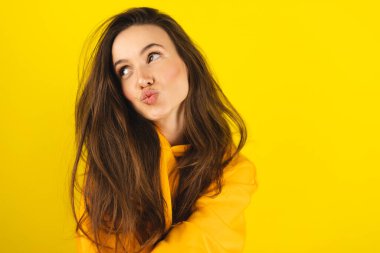 Sarı kapüşonlu giyen mutlu bir kadın sarı stüdyoya hava öpücüğü gönderir. Çekici kız öpücük yolluyor. Kadın özgürlüğü yaşam tarzı. Çekici şıklığın kameraya öpücüğü göndermesi. Kadın aşk hikayesi. Duygu..