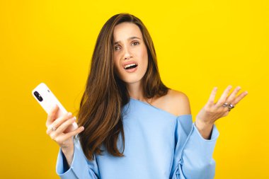 Sarı arka planda izole edilmiş cep telefonu kullanan genç ve güzel bir kadın. Bağıran mutsuz kadın cep telefonunu tutuyor. Hayal kırıklığına uğramış üzgün bayan, haberleri dehşete düşürdü. Bu da ne? Olamaz.
