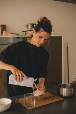 Evde, mutfakta matcha latte yaparken bir kadın, karton kutudan bardağa süt döker..