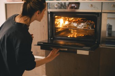 Genç bir kadın fırına terbiye edilmiş tavuk koyuyor. Kız fırını açıyor.. 