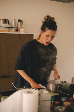 Pişirdikten sonra kirli elektrik indüksiyon sobası, süt biter, kadın sobayı kağıt havluyla yıkar, tencere tavayı sütle tutar. Mutfakta karışıklık. Kadın bağırıyor ve kızgın görünüyor, problemden mutsuz..