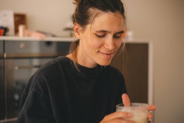 Mutfakta duran bir kadın, elinde bir bardak ılık süt, içecek ve lezzetin tadını çıkarıyor, kokla..