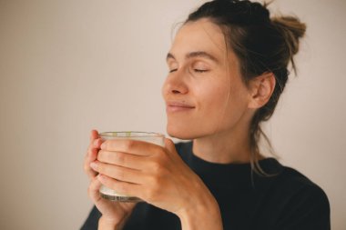 Rahatlamış genç bir kadın sabahları evde sütlü sütlü sütlü çayını kokluyor. Topuzlu kız siyah bluz giyiyor..