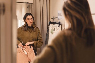 Modern genç bayanın, elbise mağazasında nasıl giyindiğini değerlendirme fırsatı var. Şık kıyafetler. Alışveriş ve zevk. Kotunu kendine yakın tut ve aynaya bak..