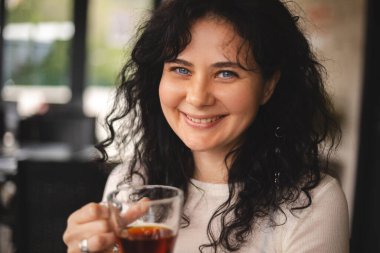 Kahvede oturan mutlu esmer, kıvırcık kadın, biriyle güzel bir sohbet ettiğinde, çayın tadını ve kokusunu alır. Beyaz giysili kadın çay içiyor, gülümsüyor.. 