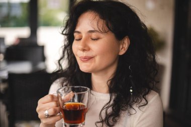 Kahvede oturan mutlu esmer, kıvırcık kadın, biriyle güzel bir sohbet ettiğinde, çayın tadını ve kokusunu alır. Beyaz giysili kadın çay içiyor, gülümsüyor.. 