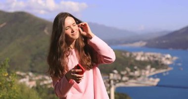 Mutlu esmer, uzun saçlı, dağ ve denizin karşısında duran, kablosuz kulaklıkla müzik dinleyen, şarkı söyleyen, dans eden, saçını düzelten, cep telefonu tutan, pembe uzun kollu kadınlar..