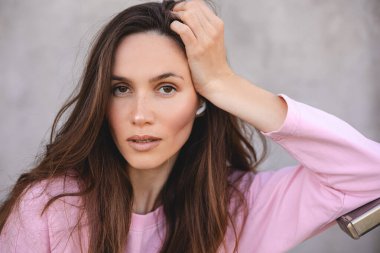 Güzel esmer, uzun saçlı kadının portresi pembe uzun kollu gömlek giyiyor, başını tutuyor ve merdivenlerin yanında duruyor. Kulaklıklı beyaz kız, müziği dinle..