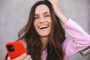 Çekici, neşeli, şaşkın kız cihaz uygulaması kullanıyor, SMS, gönderi, sosyal medya haberleri paylaşıyor. Elinde alet tutan, mesaj atan, mesaj atan olumlu bir kadın. Kız pembe uzun kollu kazak giyiyor..
