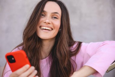 Çekici, neşeli, şaşkın kız cihaz uygulaması kullanıyor, SMS, gönderi, sosyal medya haberleri paylaşıyor. Elinde alet tutan, mesaj atan, mesaj atan olumlu bir kadın. Kız pembe uzun kollu kazak giyiyor..