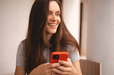 Cep telefonu tutan ve evin yanında otururken akıllı telefona bakan genç ve güzel bir kadın. Mutlu kız cep telefonu kullanıyor ve flört ediyor. Gülümseyen kadın telefonu tut, iyi haberler oku, mesaj bırak..