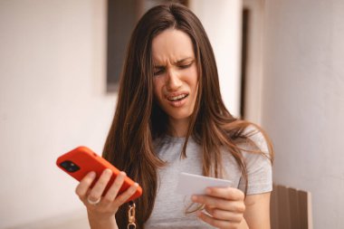 Kumral, uzun saçlı, kısa saçlı bir kadın kredi kartı kullanıyor. Akıllı telefon, e-ödemeyle ilgili sorunlar yaşıyor. Parasızlık, ödeme güvensizliği, yetersiz fonlar yüzünden kendini rahatsız hissediyor. Dolandırıcılık mağduru..