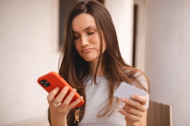 Kumral, uzun saçlı, kısa saçlı bir kadın kredi kartı kullanıyor. Akıllı telefon, e-ödemeyle ilgili sorunlar yaşıyor. Parasızlık, ödeme güvensizliği, yetersiz fonlar yüzünden kendini rahatsız hissediyor. Dolandırıcılık mağduru..