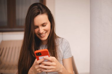 Cep telefonu tutan ve evin yanında otururken akıllı telefona bakan genç ve güzel bir kadın. Mutlu kız cep telefonu kullanıyor ve flört ediyor. Gülümseyen kadın telefonu tut, iyi haberler oku, mesaj bırak..