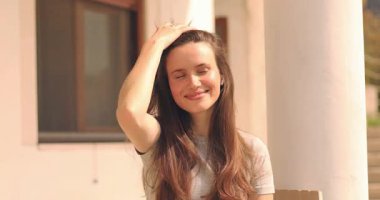 Sevimli esmer kadın, şakacı bir şekilde göz kırpıyor, flört ediyor. Kadınlar sabah evin yanında oturarak saçlarını düzeltirler. Esmer, manken suratlı, gülümseyen. Kız etrafına bak, elini sallıyor..