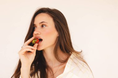 Güzel, çekici, çekici, çekici, dalgalı saçlı, ısıran, çilek yiyen bayanın portresi. Parlayan cilt için sağlıklı beslenme, cilt bakımı ve su kaybı.. 
