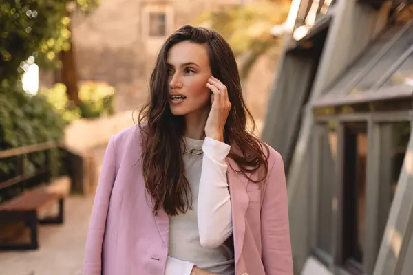 Açık havada gülümseyen uzun saçlı, pembe ceketli ve beyaz tişörtlü çekici bir genç kadın. Şehir yaşam tarzı, doğal güzellik, günışığında moda portresi. El ele tutuşun..