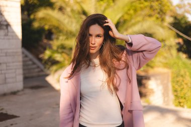 Harika uzun dalgalı, esmer, saçlı, cilveli bir kadının haftasonunu dışarıda yürürken çekilmiş bir fotoğraf. Pembe ceket ve beyaz uzun kollu tişört giy.. 