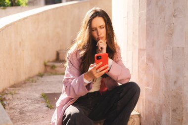 Elini çenesinde tutarken telefonu tutan bir kadın. Kampüs dışında düşünen etkileyici bir öğrenci, elinde akıllı telefon olan kuşkulu bir kadın bilgi okumayı, arama çözümü bulmayı düşünüyor..