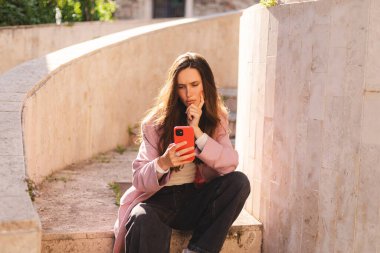 Elini çenesinde tutarken telefonu tutan bir kadın. Kampüs dışında düşünen etkileyici bir öğrenci, elinde akıllı telefon olan kuşkulu bir kadın bilgi okumayı, arama çözümü bulmayı düşünüyor..