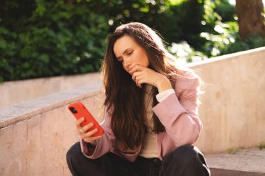 Elini çenesinde tutarken telefonu tutan bir kadın. Kampüs dışında düşünen etkileyici bir öğrenci, elinde akıllı telefon olan kuşkulu bir kadın bilgi okumayı, arama çözümü bulmayı düşünüyor..