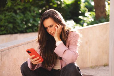 Elini çenesinde tutarken telefonu tutan bir kadın. Kampüs dışında düşünen etkileyici bir öğrenci, elinde akıllı telefon olan kuşkulu bir kadın bilgi okumayı, arama çözümü bulmayı düşünüyor..