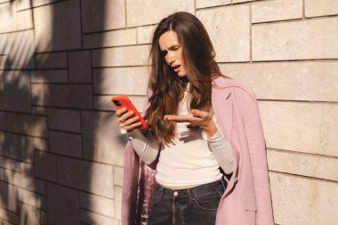 Duvar ofis binasının yanında cep telefonu kullanan çılgın ve şok edici esmer bir kadın. Bağıran mutsuz kadın cep telefonunu tutuyor. Hayal kırıklığına uğramış üzgün bayan, haberleri dehşete düşürdü. Bu da ne? Olamaz.