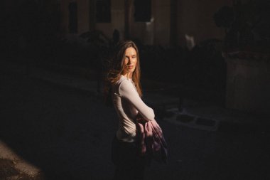 Beyaz bluzlu genç bir kadın sıcak bir akşam güneşi altında elinde pembe bir ceketle dikiliyor. Onun ifadesi hayalperest ve düşünceli. Sahne rahat ve içten geliyor..