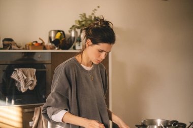 Kadın mutfaktaki ocağın yanında duruyor, tencerede yemeğinin güzel kokularını pişiriyor ve kokluyor. Ev hanımı öğle yemeği ya da kahvaltı hazırlıyor..