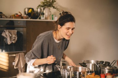 Güzel, mutlu, genç bir kadın mutfakta yemek pişiriyor ve ocaktaki tavadan biraz aroma kokusu geliyor. Mutfakta yemek pişiren kadın tencerede karıştırıyor akşam yemeği hazırlıyor. Genç ev hanımı gülümsüyor