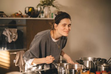 Güzel, mutlu, genç bir kadın mutfakta yemek pişiriyor ve ocaktaki tavadan biraz aroma kokusu geliyor. Mutfakta yemek pişiren kadın tencerede karıştırıyor akşam yemeği hazırlıyor. Genç ev hanımı gülümsüyor