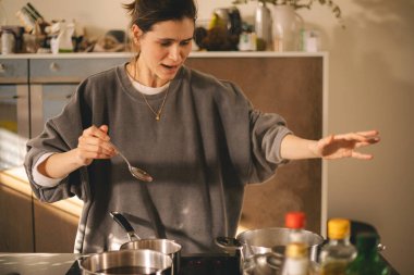 Mutfakta afete uğrayan genç bir ev hanımı şoka girdi ve akşam yemeği hazırladı. Acelesi olan kadın, üzgün ve kızgın görün..