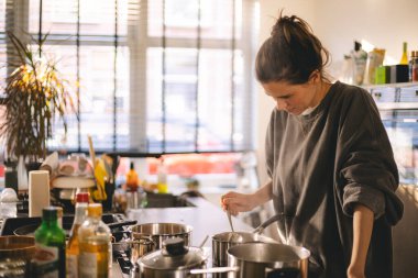 Kadın mutfaktaki ocağın yanında duruyor, tencerede yemeğinin güzel kokularını pişiriyor ve kokluyor. Ev hanımı öğle yemeği ya da kahvaltı hazırlıyor..