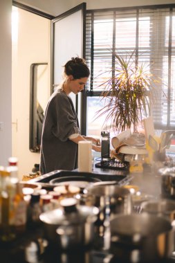 Modern, rahat bir mutfak masasında duran ev hanımı, masa örtüsünü mikrofiber bezle siler, profesyonel temizlik ürünlerini ev temizliği ve temizlik konsepti için kullanır. Esmer kadın yemek ve temizlik yapıyor..