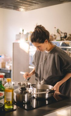 Kadın mutfaktaki ocağın yanında duruyor, tencerede yemeğinin güzel kokularını pişiriyor ve kokluyor. Ev hanımı öğle yemeği ya da kahvaltı hazırlıyor..