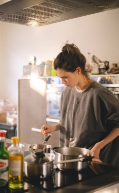 Kadın mutfaktaki ocağın yanında duruyor, tencerede yemeğinin güzel kokularını pişiriyor ve kokluyor. Ev hanımı öğle yemeği ya da kahvaltı hazırlıyor..