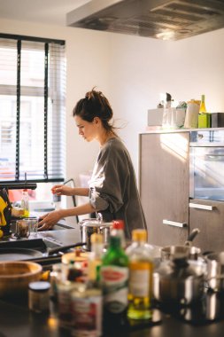 Modern, rahat bir mutfak masasında duran ev hanımı, masa örtüsünü mikrofiber bezle siler, profesyonel temizlik ürünlerini ev temizliği ve temizlik konsepti için kullanır. Esmer kadın yemek ve temizlik yapıyor..