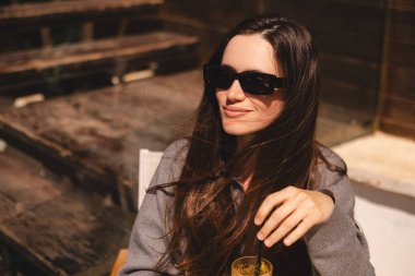 Kafede oturup portakallı limonata, taze meyve suyu ya da kokteyl içen uzun saçlı mutlu esmer. Susuzluğunu giderir. Rahatlama konsepti. Gülen mutlu kadın soğuk kokteyl içiyor..