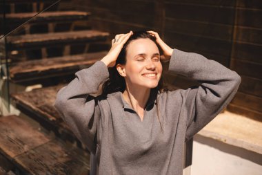 Şirin esmer, uzun saçlı, gülümseyen, saçını düzelten, gözlerini kapatan bir kız. Kadın saçını düzeltiyor. Gri kazak giyiyor, kafede dinleniyor. Mutlu esmer kız flört ediyor ve cilveleşiyor..